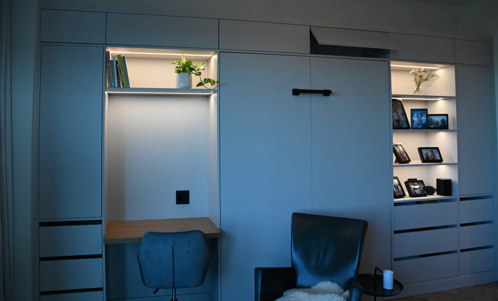 Slate-blue cabinetry with a contrasting wood desk and warm shelf light